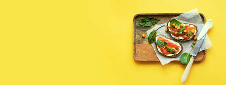 Breakfast starts a brisk day. Sandwich with slightly salted salmon, chickpeas and seasonal herbs. Healthy eating concept. On the tray is a snack and a knife with butter, a bright yellow background.の写真素材