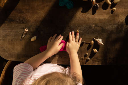 The girl plays with salty pink dough on the kitchen table. Hands mold clay with their own hands to create homemade zero-waist toys. Creative lesson with a test of natural products. Development of children in the period of self-isolation.の写真素材