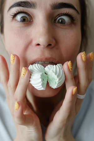 Young woman eating marshmallow. Pretty caucasian woman smiling. Sincere emotions. facial...