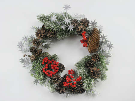 Christmas wreath of pine and spruce cones, red berries, pine branches, and a garland of shiny leaves on a white background. Winter holiday Xmas and New Year. View from aboveの写真素材