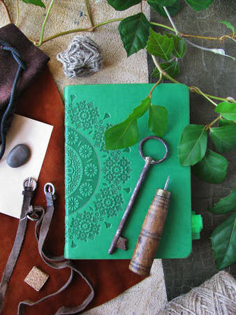 A green notebook with a pattern, an old key, and craft suppliesの写真素材