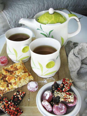 A piece of pie with jam, sweets, two cups of tea, and teapotの写真素材