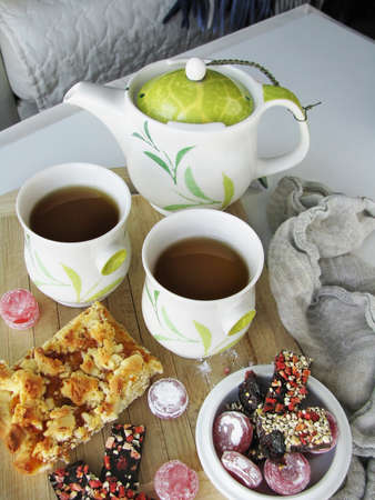 A piece of pie with jam, sweets, two cups of tea, and teapotの写真素材