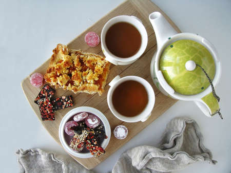 A piece of pie with jam, sweets, two cups of tea, and a teapot on a wooden board. View from aboveの写真素材