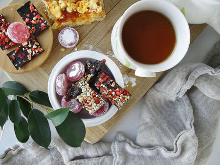 A cup of tea, sweets, and sprig with green leaves on the tableの写真素材