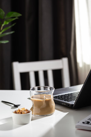 Coffee in a glass cup on a white table with a laptopの写真素材