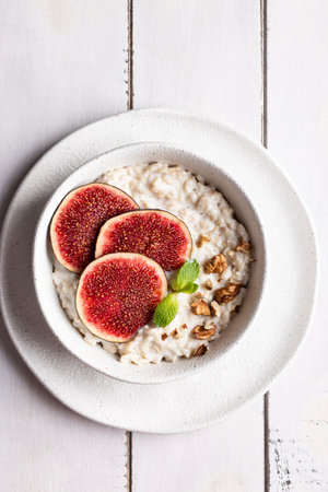 Oatmeal with fresh figs and walnuts on white wooden backgroundの写真素材