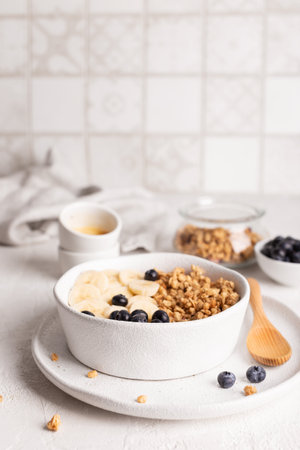 Healthy breakfast. Oatmeal with banana, blueberry and granola in a bowl on a light background.の写真素材
