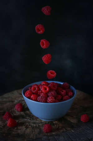flying raspberries over a plate on a dark backgroundの写真素材