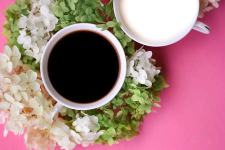 black coffee mug and milk mug with white flowers on pink backgroundの写真素材