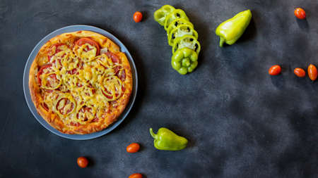 vegetarian pizza and green peppers with cherry tomatoes on a dark backgroundの写真素材