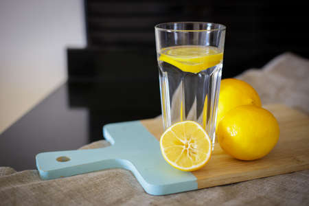 glass cup with water and lemon on a wooden board for slicingの写真素材