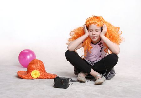 Beautiful little redheaded girl / child listening to disco music with headphones against white backgroundの写真素材
