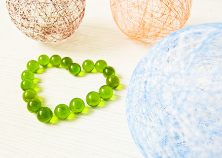 balls of yarn of different colors on a light background, heart of green glass beadsの写真素材
