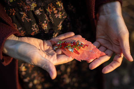 In women's hands is an autumn leaf of autumn and a hair accessory made of glass beads. The concept of autumn. Close-up photoの写真素材