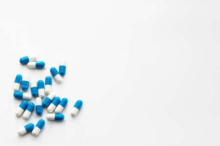 Scattered white and blue pills on white table. Mock up for special offers, advertising, web background. Medical, pharmacy and healthcare concept. Copy space. Empty place for text or logo.の写真素材