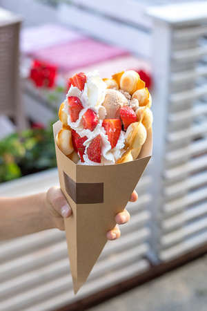 Large beautiful ice cream in Belgian waffle decorated with strawberries and cream in craft paper on...
