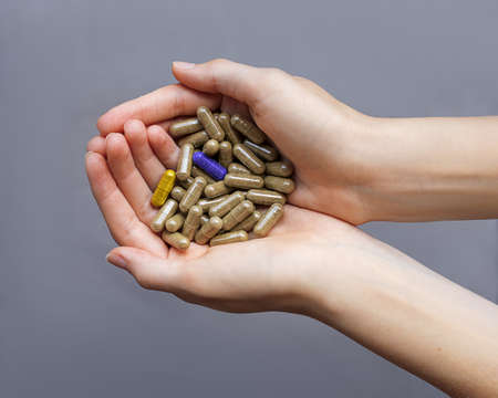 Among the faceless capsules without color in the hands of women are two bright capsules. Conceptual close-up photo. Be not like everyone else. Be yourself. ealthy lifestyle. Make choiceの写真素材