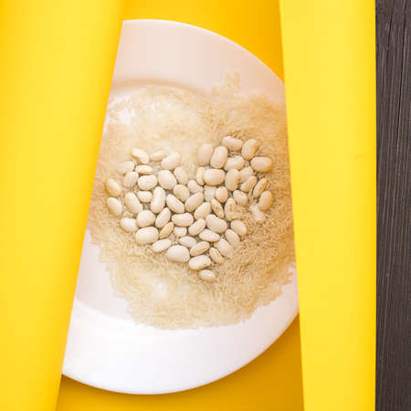 Photo concept of love for vegetarian food. Heart of beans on a white plate with rice in yellow paper. close up. Healthy lifestyle. Natural and healthy foodの写真素材