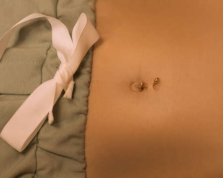slender female tummy, navel piercing, bow. Sexy close-up warm photo.の写真素材
