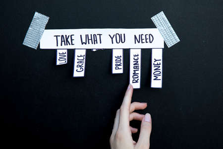 ad with the inscription Take what you need. A woman's caucasian hand reaches for one of the words to make a choice love grace romance pride money. Photo for your articles about psychology, lifestyleの写真素材