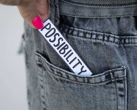 A beautiful woman's hand with bright manicure takes a paper with the inscription Possibility from the pocket of her jeans. Photo for an article on psychology, coaching or motivationの写真素材