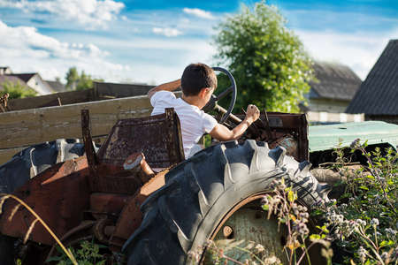 A 10-year-old school-age boy tries to start an old tractor or car. Repair. Little helper. Harvest time. Raising sons by a father. Photo. Family farmerの写真素材