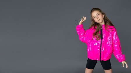 A beautiful long-haired school girl in a fashionable bright pink raincoat with hood poses on a gray background. Free space for text, copy spaceの写真素材