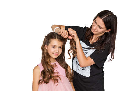 A hairdresser makes a hairstyle for beautiful 10-year-old girl with long curly hair. Studio photo...
