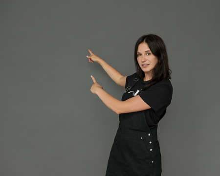 A beautiful young female programmer, teacher points to an empty space on a gray background for your text. Fashionable casual clothing, natural look. The concept presentation, staff trainingの写真素材