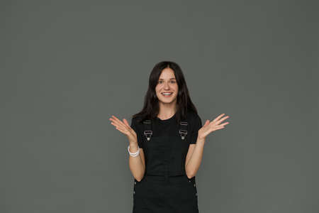 A beautiful young woman is excited, surprised, happy. She spreads her hands, smiles. Studio photo on a gray background. Message to client. Copy space for text. The concept of emotional advertisingの写真素材