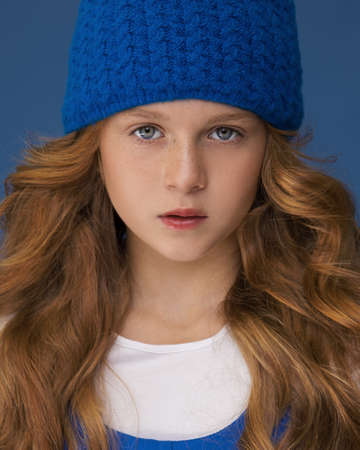 Winter hat styles. Kid girl wear knitted hat. Winter accessory concept. Girl long hair blue background. Cold season. Winter fashion accessory. Teen wearing warm cloth. Style guide. Close-up photoの写真素材