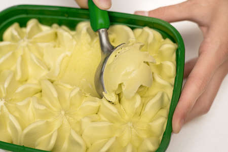 A scoop of tender green pistachio ice cream with pistachios, mint apples and lemon in a special spoon in the hands of a young girl. Concept of kitchen appliances, sweet life. Close-up photoの写真素材