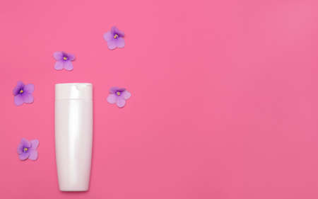 Skin care packaging mockup on a pink background among violet flowers. Flat lay. Cosmetic beauty natural. Face and body treatment. Copy space. Top viewの写真素材