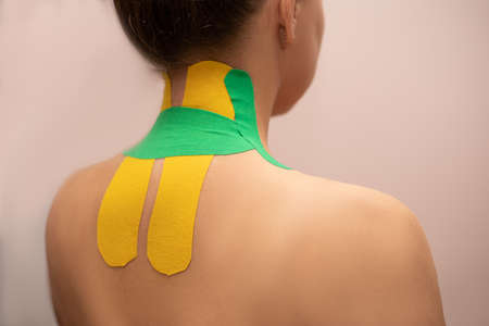 A young woman with a bright kinesiotherapy tape with on the shoulder and back at the therapist's...