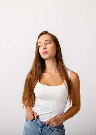 A beautiful young slender long haired brunette girl holds her jeans and looks thoughtfully to the...