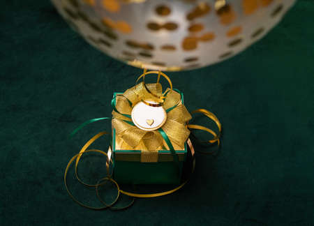 Green gift with gold bow with shiny decor ballwoon with little heart on dark background with christmas light. Holiday consept. Copy space. Photoの写真素材