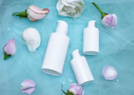 Top view of mock-up of white squeeze bottle plastic tube and roses on blue background. Bottle for...