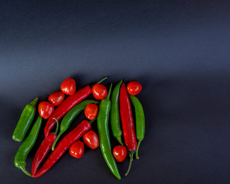 Top view on cherry tomatoes and mini red hot chili peppers in old plate on dark wooden table. Dark food photography with bunch of red chili and tomatoes. Photoの写真素材