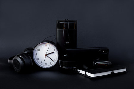 Black business accessories on a black background. Stationery. Watch notebook mobile headphones pen....