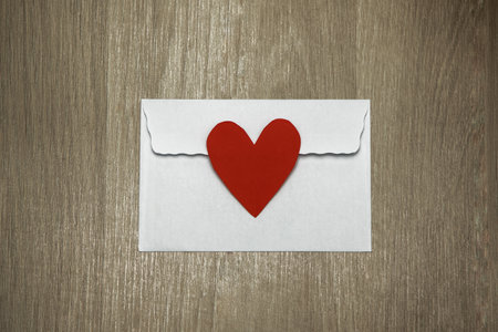 White envelope with red valentine heart on wooden background. Flat lay, close-up photo, mock up....