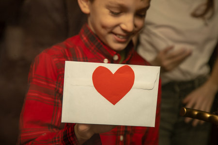 Boy glues to window envelope with valentine for his girlfriend. Preparing surprise. Authentic view...