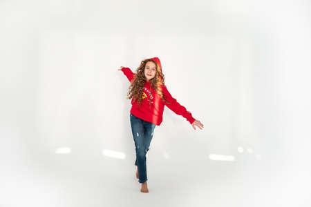 Funny young curly brunette girl in casual red hoodie jeans runs on white background. Teenagers lifestyle concept. Copy space. Runningの写真素材