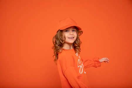 Beautiful child girl 6-7 years old in orange cap with place for text, mock up. Showing hand, Studio shot, Printing on textiles, production of hatsの写真素材