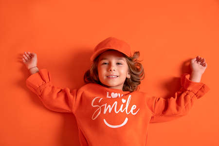 Smiling little child girl 6-7 years old in cap and fashionable clothes lies on floor in the studio...