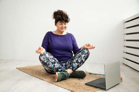 Senior Woman sitting on exercise mat lotus position with her eyes closed doing yoga homeの写真素材