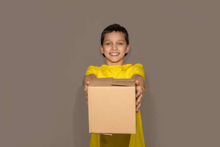 Smiling young delivery teen boy holding and carrying a cardboard box package on gray background in studioの写真素材