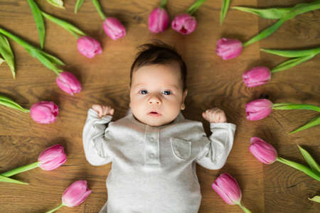 Photo of newborn baby boy or girl lies among tulips and looking into the frame. Great greeting cardの写真素材