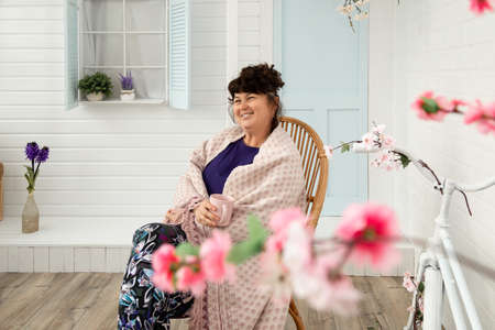 Attractive happy smiling middle aged woman sitting on wicker chair in backyard. Summer and spring...
