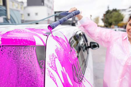 Caucasian woman washing car at self-serve car wash with pink foam, stock photoの写真素材